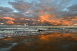 Warm, roze licht van de zon schijnt op een wolkenlucht boven zee tijdens zonsopkomst op het strand van Bloemendaal aan Zee
