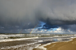 Regenboog aan de onderkant van een hagelbui op het strand van de Noordduinen bij Callantsoog